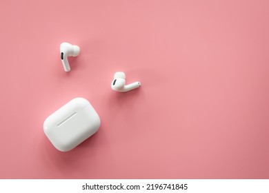 Wireless in-ear headphones with a case on a pink background, flat lay.