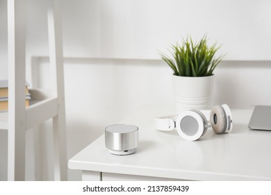 Wireless Portable Speaker And Headphones On Table Near Light Wall