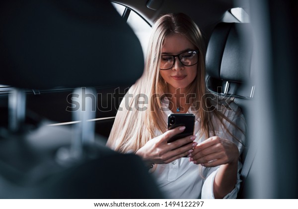 Wireless technologies. Smart\
businesswoman sits at backseat of the luxury car with black\
interior.