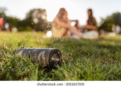wireless waterproof speaker on foreground of company of friends having fun together in park listening to music