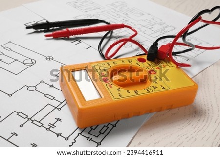 Wiring diagrams and digital multimeter on white wooden table, closeup