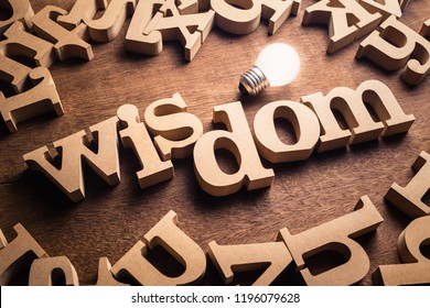 Wisdom word in scattered wood letters with glowing white light bulb, power of wisdom
