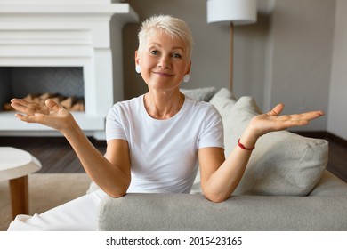 Wise senior female with calm smile on couch throwing up hands in despair. Something went wrong, fail of plans, ruined day. It is what it is, acceptance, go with flow concept
