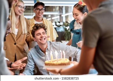 Wish you all the best. Young cheerful man is going to blow candles on cake and make a wish while celebrating birthday with colleagues. Birthday concept. Corporate party - Powered by Shutterstock