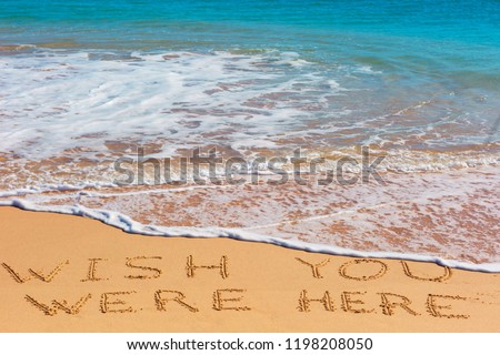 WISH YOU WERE HERE insctiption on wet beach sand with the turquoise sea on background. Summer season  vacation concept.