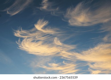 Wispy windblown cloud formations backlit by setting sun against darker blue sky natural horizontal background pattern