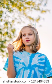 Wistful, nostalgic image of a young girl playing with her hair.  Looking up at the girl as she twirls her hair.  Backlit.  Bokeh in trees from film lens used on a digital camera.  She has blue eyes.