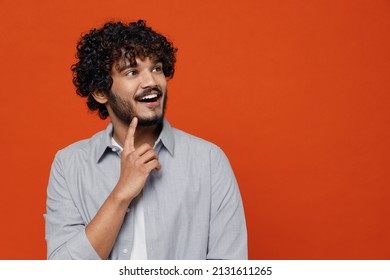 Wistful young bearded Indian man 20s wears blue shirt put hand prop up on chin lost in thought and conjectures isolated on plain orange background studio portrait. People emotions lifestyle concept