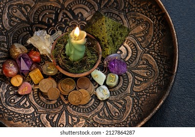 Witch altar with green candle, different old coins, stone runes, crystals on dark table background. Magic for attracting money, wealth. witchcraft money esoteric ritual. occultism concept. top view