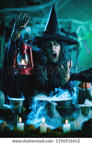 Witch with awfully face and lantern in her hand in creepy foggy surroundings sends evil. Halloween concept.