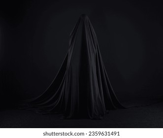 witch in a black cloak on a black background - Powered by Shutterstock