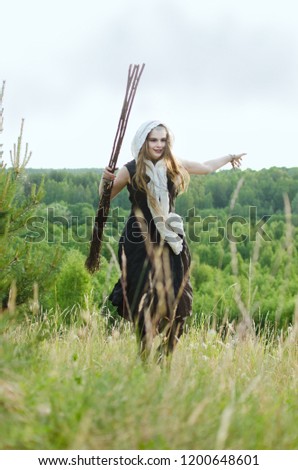 witch with a broom and a black dress to have fun in the woods on a grassy hill
