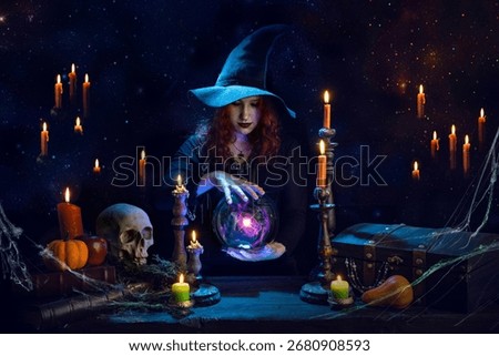 Witch casts a spell with magic Crystal ball for predictions fortune-telling. Young woman, magician girl with red hair, dressed in Halloween clothes and conical hat in a room with candles, skull