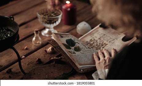 the witch cooks an elixir with herbs in a cauldron, recipe book - Shutterstock ID 1819055801