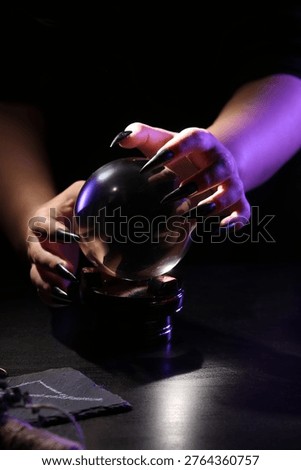 Witch with crystal ball at dark table, closeup
