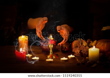Witch guessing on wax on the altar in the dark. Female hands with sharp black nails making passes above candles, pumpkin, nuts, dry leaves, magic herbs, selected focus, low key. Halloween, Yule