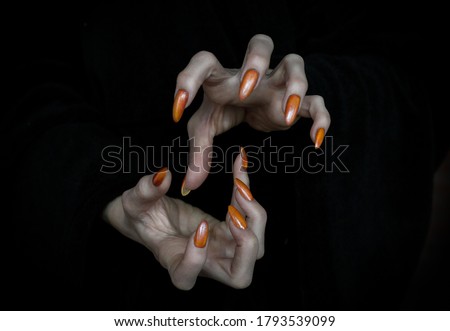 Witch hands with sharp nails and long pale fingers in the dark, low key, selected focus. Halloween, witchcraft, magic, evil, creepy and monster concept.