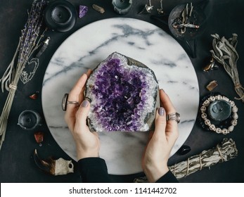The witch is holding amethyst stone surrounded magic things. View from above.