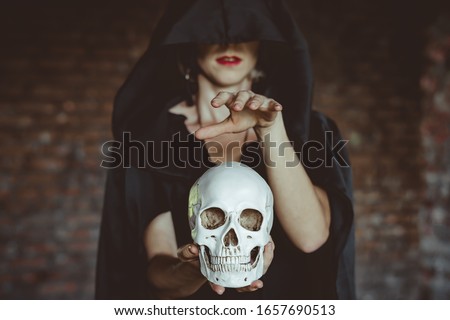 a witch holds a human skull in a black cloak in an old building