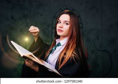 
Witch with a magic wand. A young student of the magic school conjures. The girl conjures green magic in the dark hall of the castle.