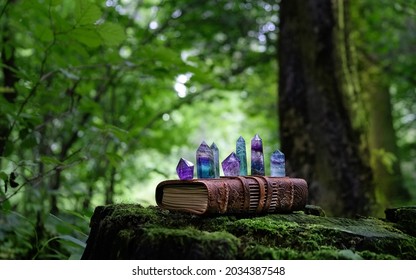 witch spell book and quartz minerals on stump in forest, natural background. Healing gemstones of fluorite and amethyst for Magic Crystal Ritual, Witchcraft, spiritual esoteric practice. reiki therapy