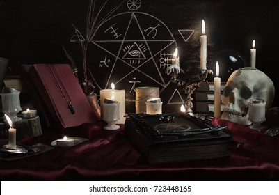 Witchcraft composition with human skull, candles, magic book and pentagram symbol. Halloween and occult concept, black magic ritual.