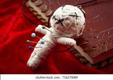 Witchcraft and place a jinx or put a spell on someone concept with a voodoo doll pierced by needles to cause harm to a victim leaning on a book of spells. Each needle represents a different curse - Shutterstock ID 716270089