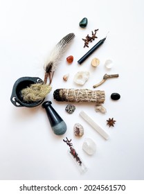 A witchy spread: cauldron, a black pestle, dried hibiscus, dalmatian jasper, celestine geodes, white quartz, selenite wand, star anise, sage bundle, polished stones, feather, twig,  and spices