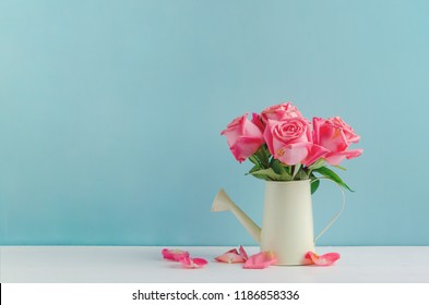 Withered pink rose flowers at watering can on white and blue wooden background with vintage tone, Vintage rose