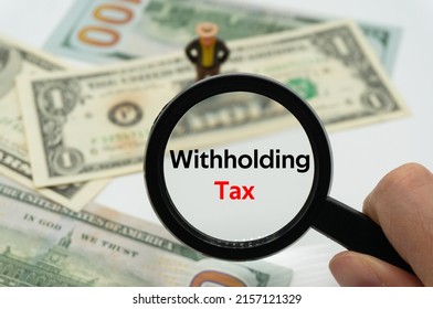 Withholding Tax.Magnifying glass showing the words.Background of banknotes and coins.basic concepts of finance.Business theme.Financial terms. - Shutterstock ID 2157121329