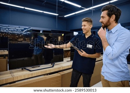 Within a contemporary electronics retail store, a young sales associate energetically demonstrates the impressive features and capabilities of a highdefinition television to an interested customer