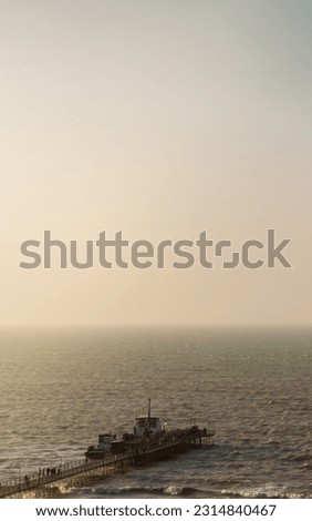 Witness the captivating beauty of a golden and hazy sunset over the ocean, as a misty atmosphere envelops a pier extending into the serene sea