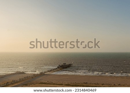 Witness the captivating beauty of a golden and hazy sunset over the ocean, as a misty atmosphere envelops a pier extending into the serene sea