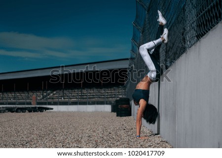 Witness woman stands on her arms at raceway handstand during racing event. 