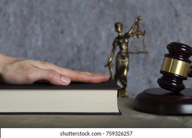 Die Hand eines Zeugen auf einer Bibel. Die Statue von Themis und das Gewölbe der Richter im Hintergrund.