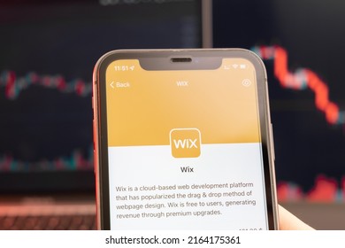 Wix stock price decrease on the trading market with downtrend line graph bar chart on the background. Man holding a mobile phone with company logo, February 2022, San Francisco, USA. 