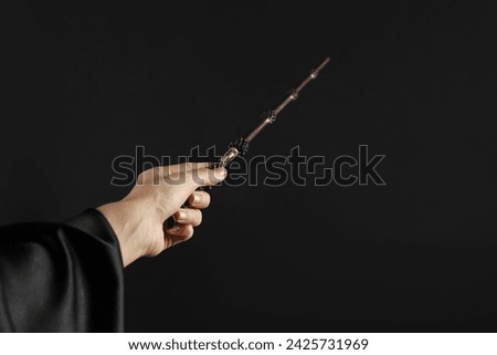 Wizard holding magic wand on black background, closeup. Space for text