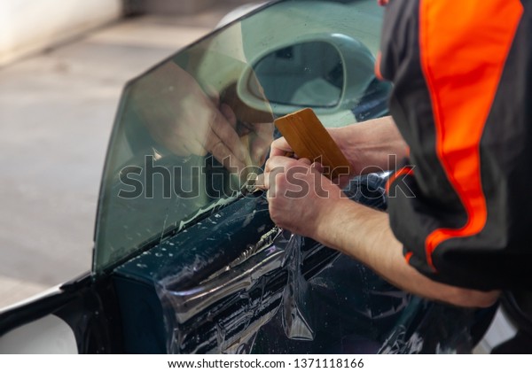 The\
wizard for installing additional equipment sticks a tint film on\
the side front glass of the car and flattens it by hand to fit the\
glass with a greenish tint in the auto\
service.