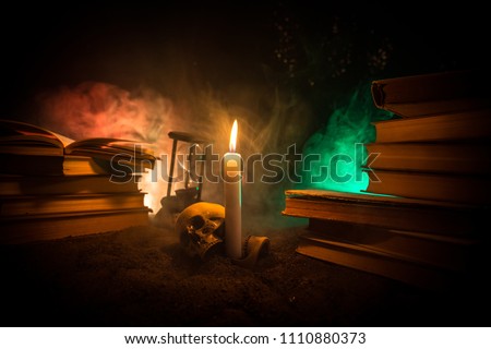 Wizard's Desk. A desk lit by candle light. A human skull, old books on sand surface. Halloween still-life background with a different elements on dark toned foggy background. Selective focus