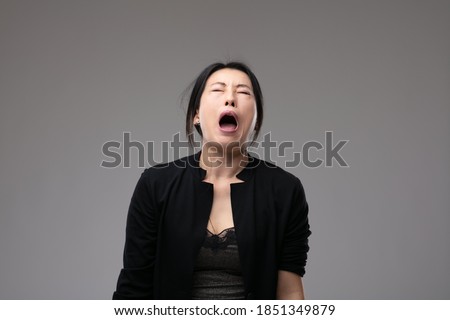 Woeful Asian woman wailing in anguish with her mouth open and a sorrowful expression over a grey studio background with copyspace