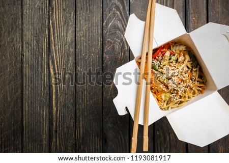 Wok noodles Udon and rice with seafood and chicken in a box on black background. With chopsticks and sauce. Asian food to go