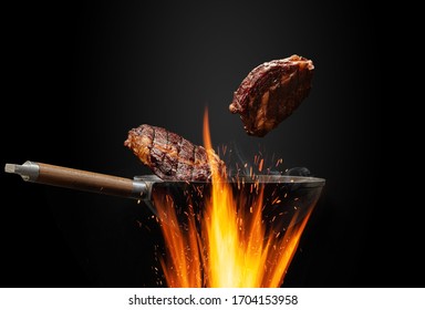 Wok Pan With Smoke Above Fire Is Frying Two Beef Steaks Against Black Studio Background. Cooking Concept. Close Up