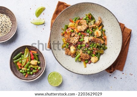 Wok with turkey meat, corn, green peas, green beans and carrots served on gray background with chopsticks. Asian food concept of street food