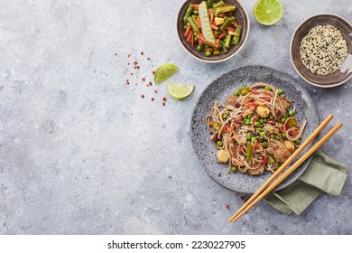Wok with turkey meat, soba noodles, corn, green peas, green beans and carrots served on gray background with chopsticks. Asian food, concept of street food. Top view with copy space - Shutterstock ID 2230227905