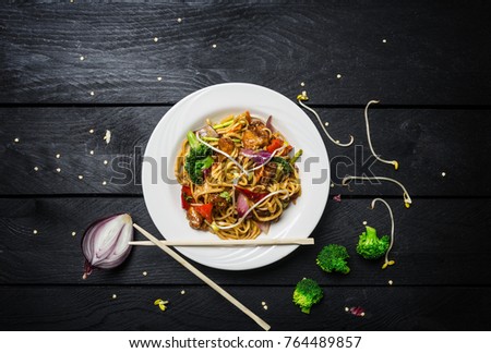 Wok. Udon stir fry noodles with chicken and vegetables in a white plate on black wooden background. With chopsticks and sauce