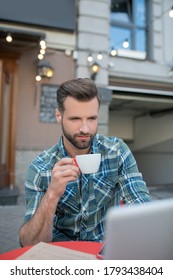 Woking Remotely. Bearded Handsome Male Ejoying Coffee, Checking His Laptop In Open Air Cafe