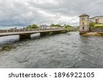 Wolfe Tone Bridge over the River Corrib with its flowing waters and the Galway Fisheries Watchtower Museum in the background, Galway Waterways, cloudy day in Galway City, Connacht Province, Ireland
