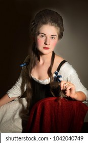 A Woman In 18th Century Stays With A High Hairstyle Sitting On A Red Chair. 