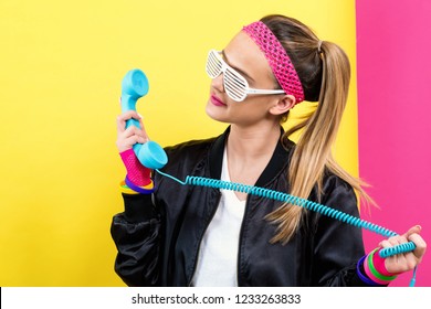 Woman in 1980's fashion with old fashioned phone on a split yellow and pink background
