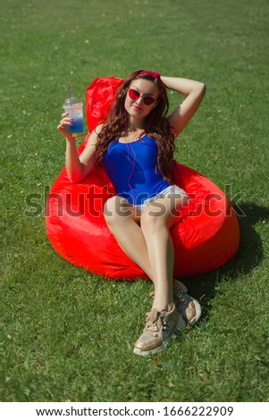 a woman of 25 years of Caucasian appearance, sunbathes in the sun, listens to music, is photographed, she is in blue body and red glasses, the concept of summer vacation